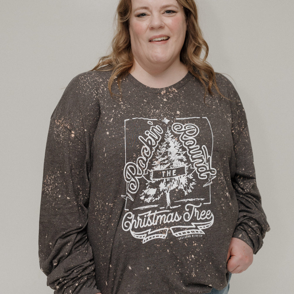 Person wearing a dark long-sleeve shirt with a Christmas tree design on a plain background