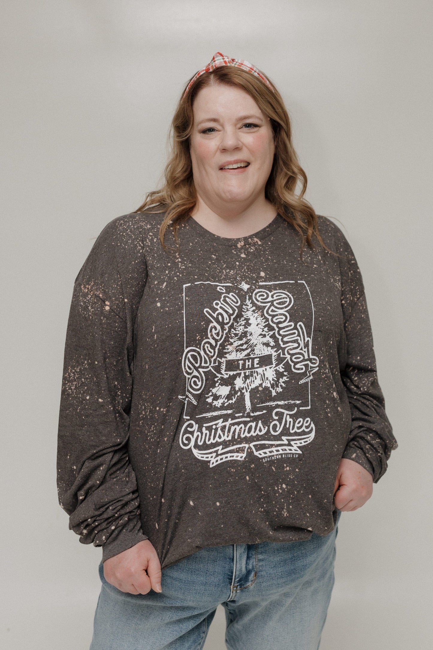 Person wearing a dark long-sleeve shirt with a Christmas tree design on a plain background