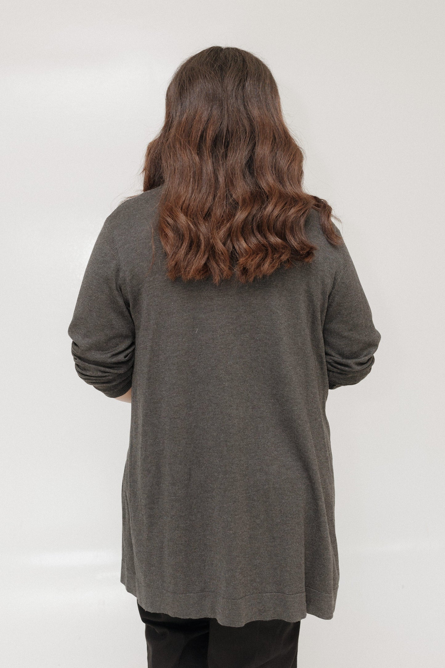 Person wearing a long gray cardigan against a white background