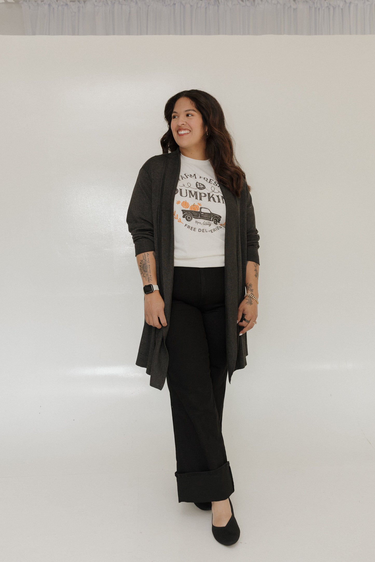 Woman wearing a graphic t-shirt, black cardigan, and black pants on a white background