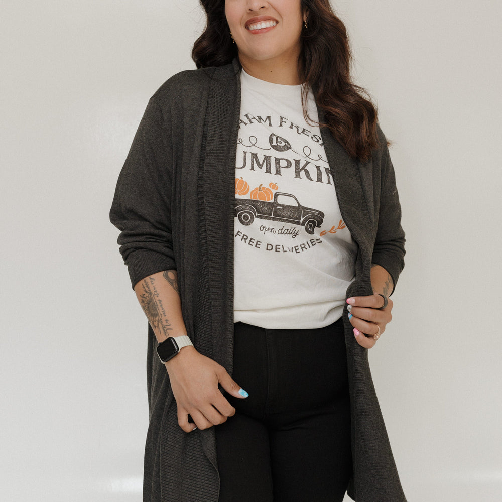 Woman wearing a graphic t-shirt with a long dark gray cardigan on a white background