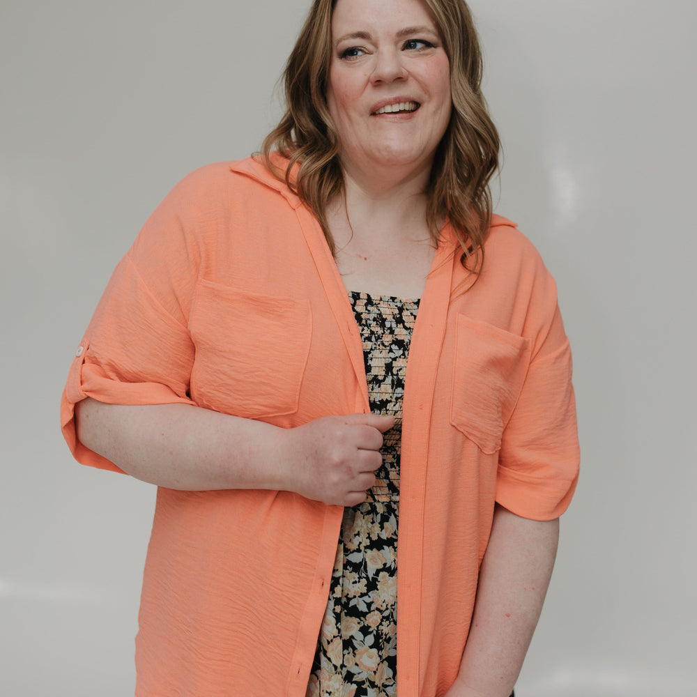 Woman wearing an orange jacket over a patterned dress against a plain background