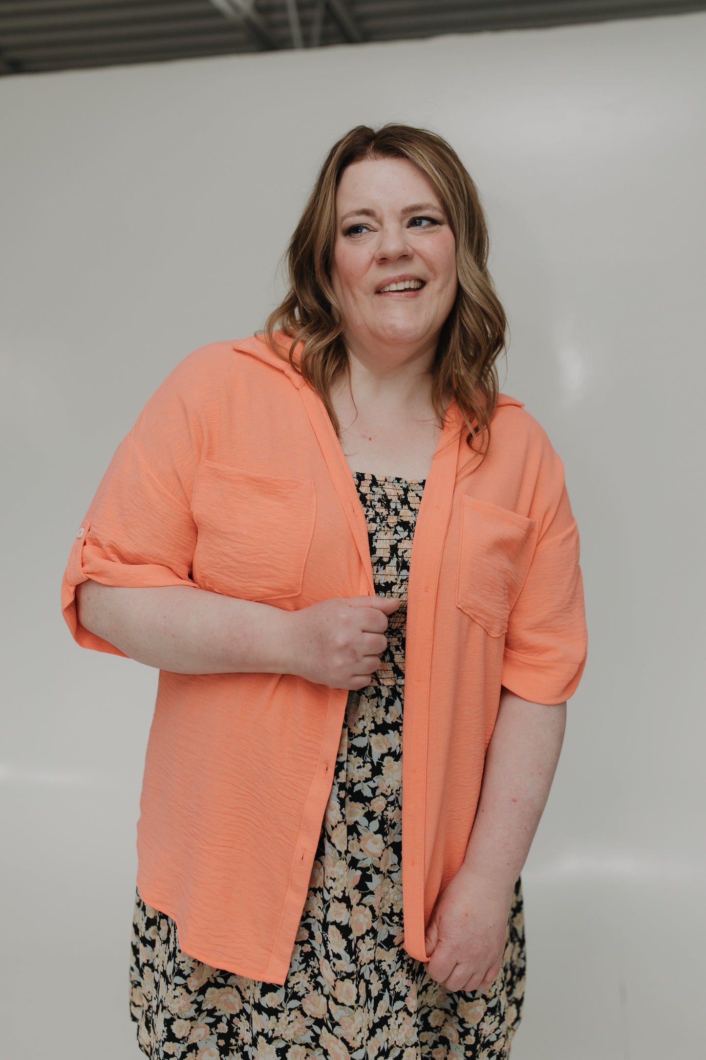 Woman wearing an orange jacket over a patterned dress against a plain background