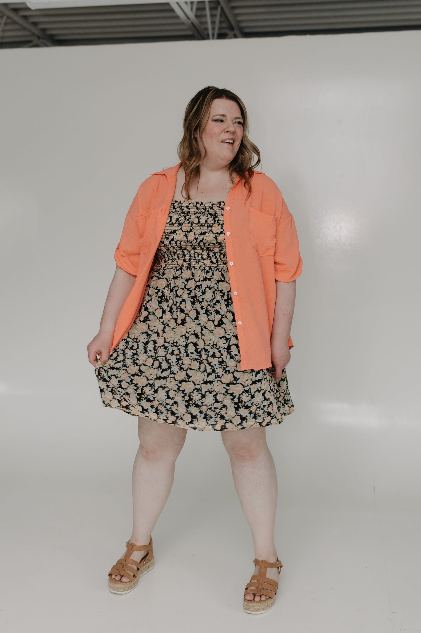 Woman wearing a floral dress with an orange cardigan against a white background