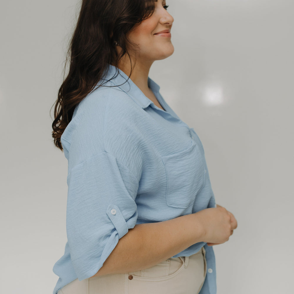 Woman wearing a light blue shirt and beige pants against a white background