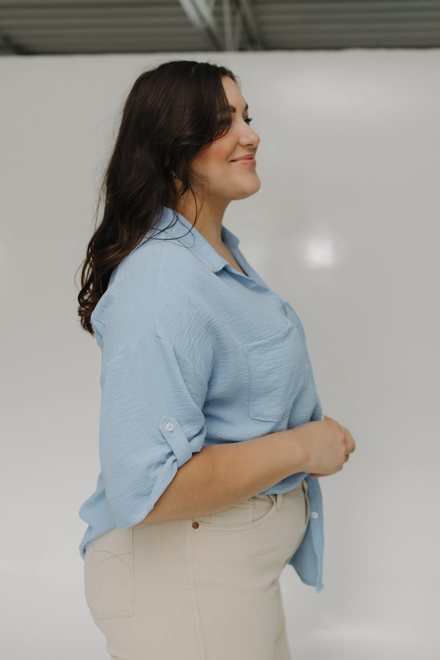 Woman wearing a light blue shirt and beige pants against a white background