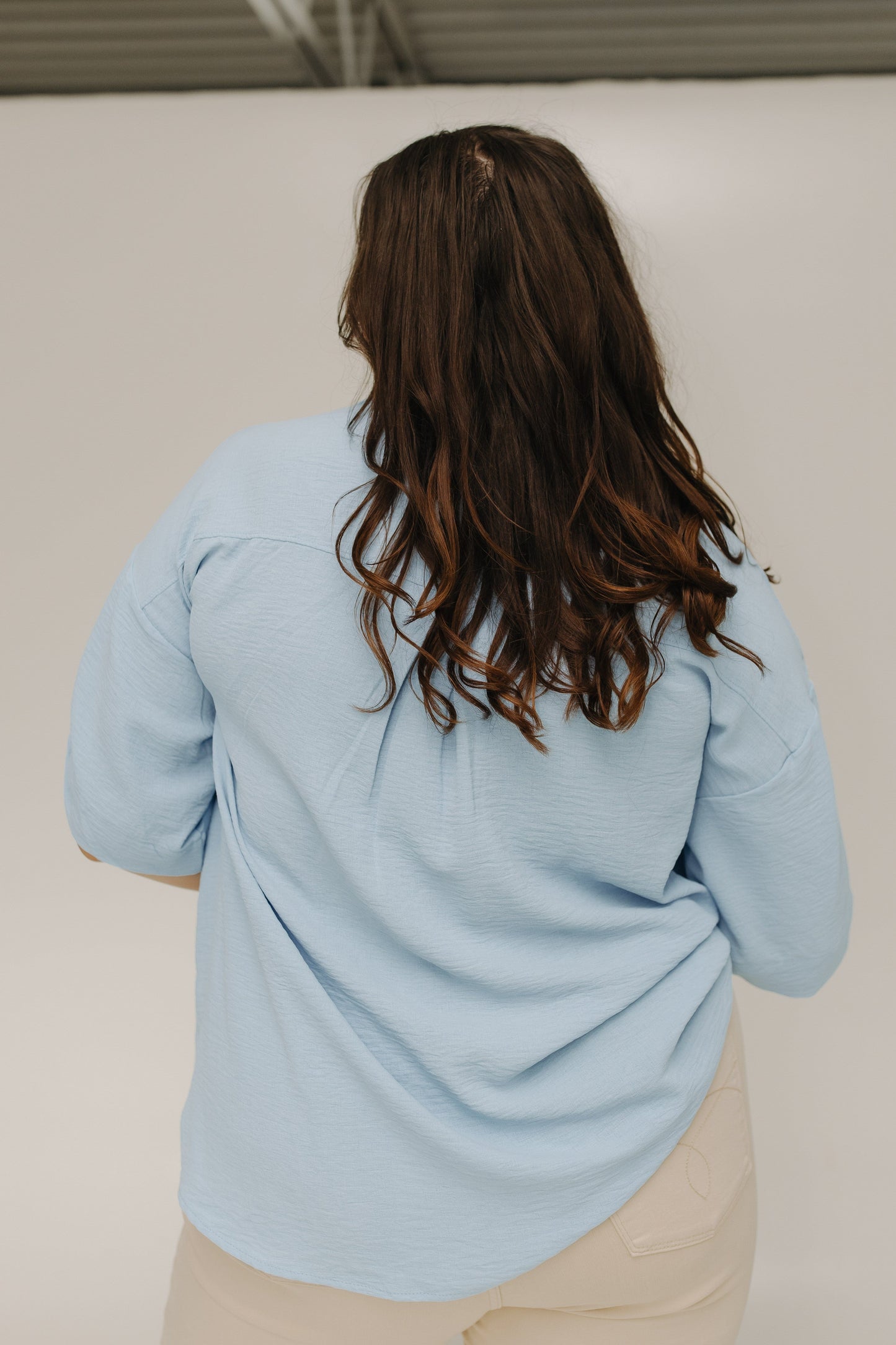 Person wearing a light blue sweater with long hair, standing against a plain background