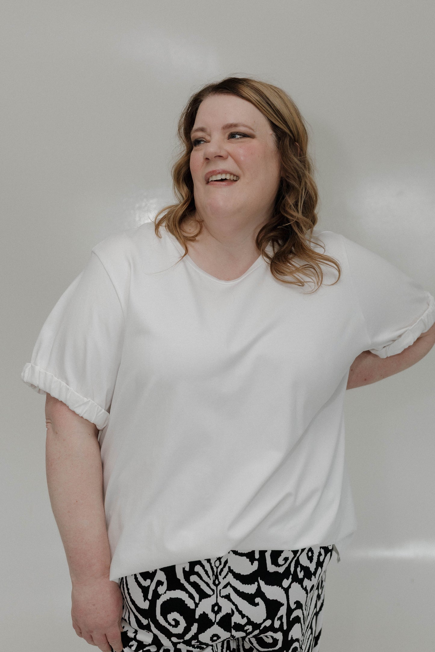 Person wearing a white t-shirt and patterned pants against a plain background