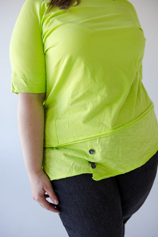 Person wearing a Love Marlow ROUND NECK TUNIC WITH BUTTON DETAIL IN TENNIS GREEN and black pants, shown from the torso down.