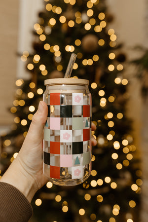 A hand delicately holds a patterned tumbler with a graceful glass straw, perfectly capturing the festive spirit in front of a twinkling Christmas tree.