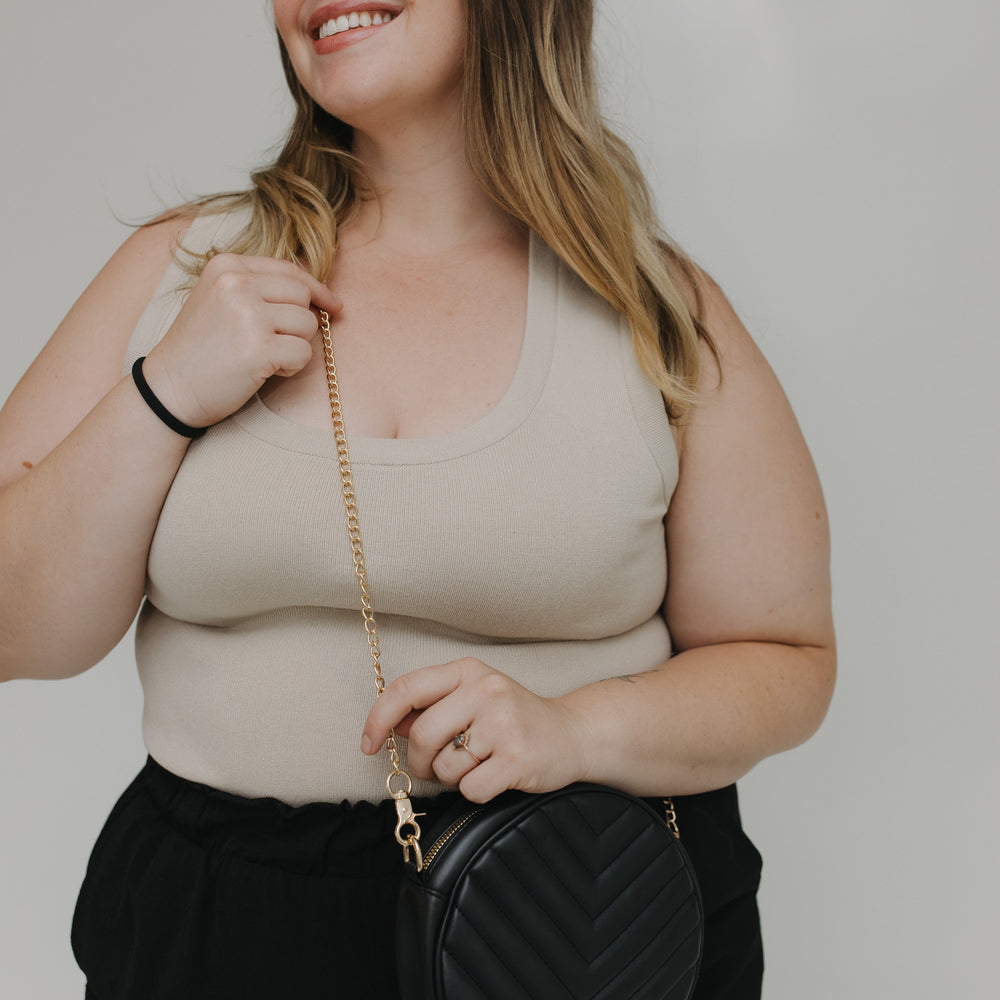 Woman holding a black handbag against a plain background