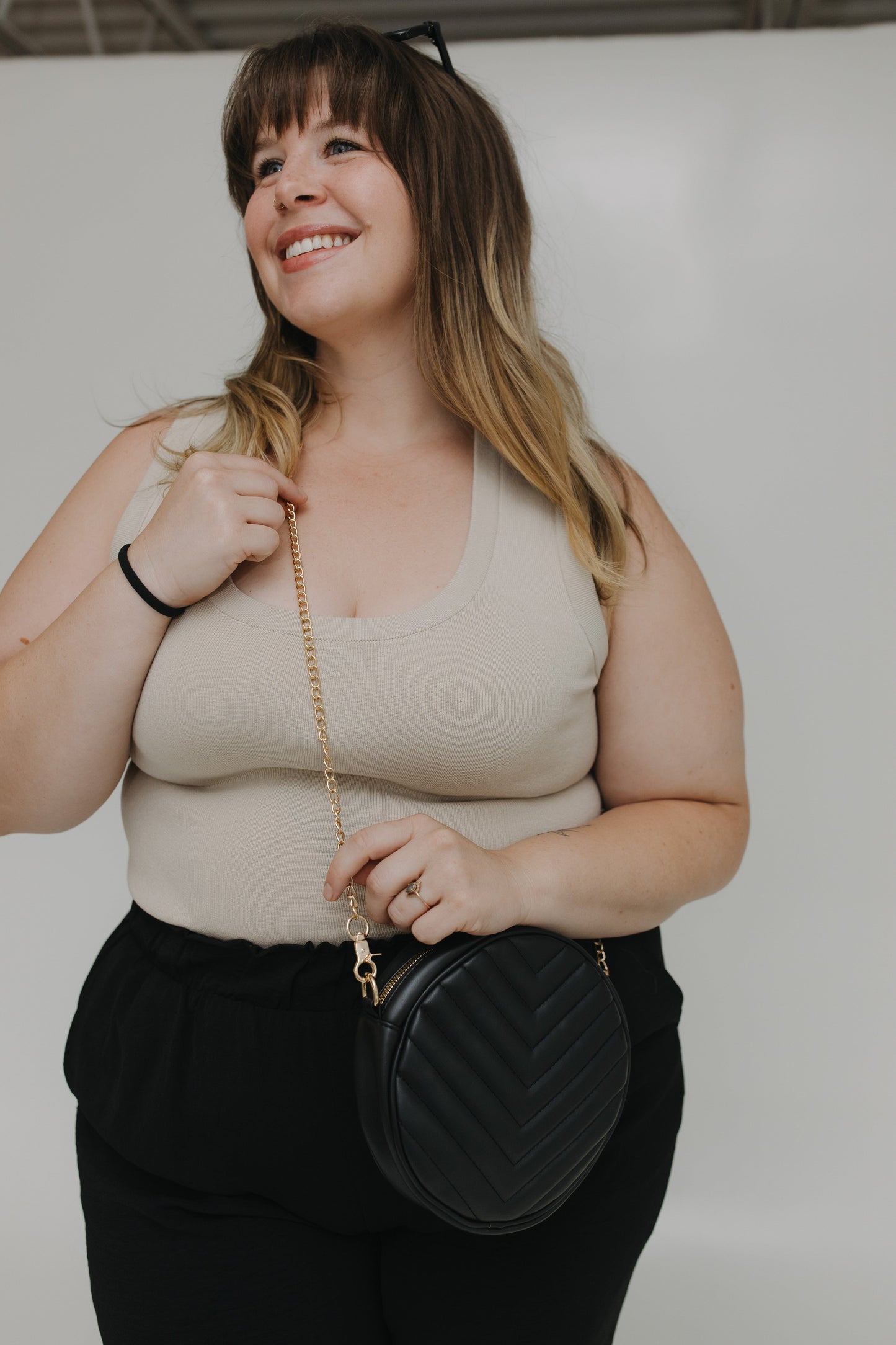 Woman holding a black handbag against a plain background