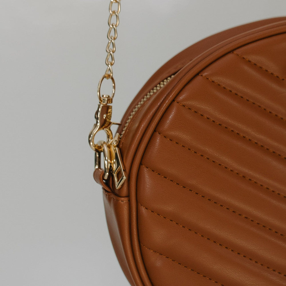 Brown leather handbag with gold chain on a light gray background