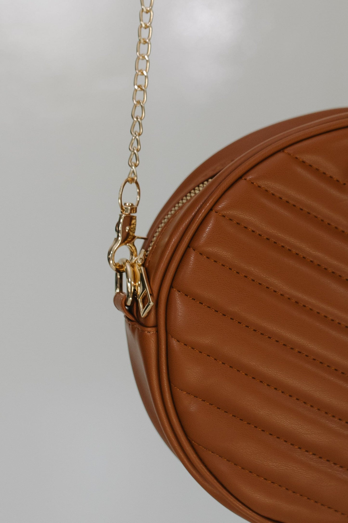 Brown leather handbag with gold chain on a light gray background