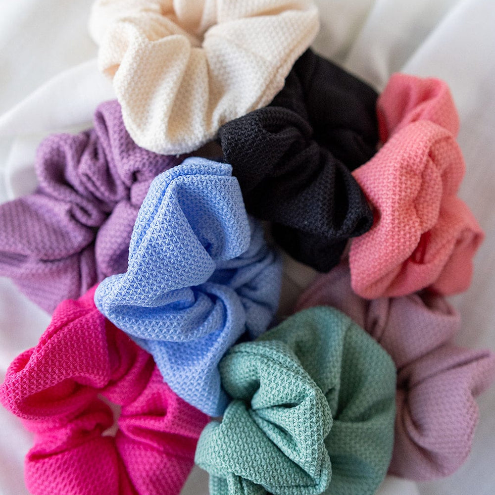 A stylish assortment of TEXTURED SCRUNCHIES IN HOT PINK, purple, black, green, blue, and cream from Love Marlow arranged on a white surface—perfect for chic ponytails.