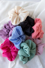 A stylish assortment of TEXTURED SCRUNCHIES IN HOT PINK, purple, black, green, blue, and cream from Love Marlow arranged on a white surface—perfect for chic ponytails.