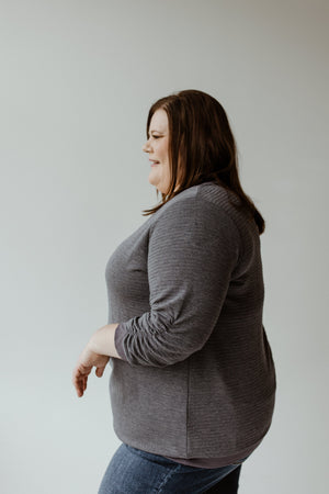 Individual wearing the Yesta 3/4 Ruched Sleeve Shimmer Top in Night Shadow and jeans, posing sideways against a plain light background.