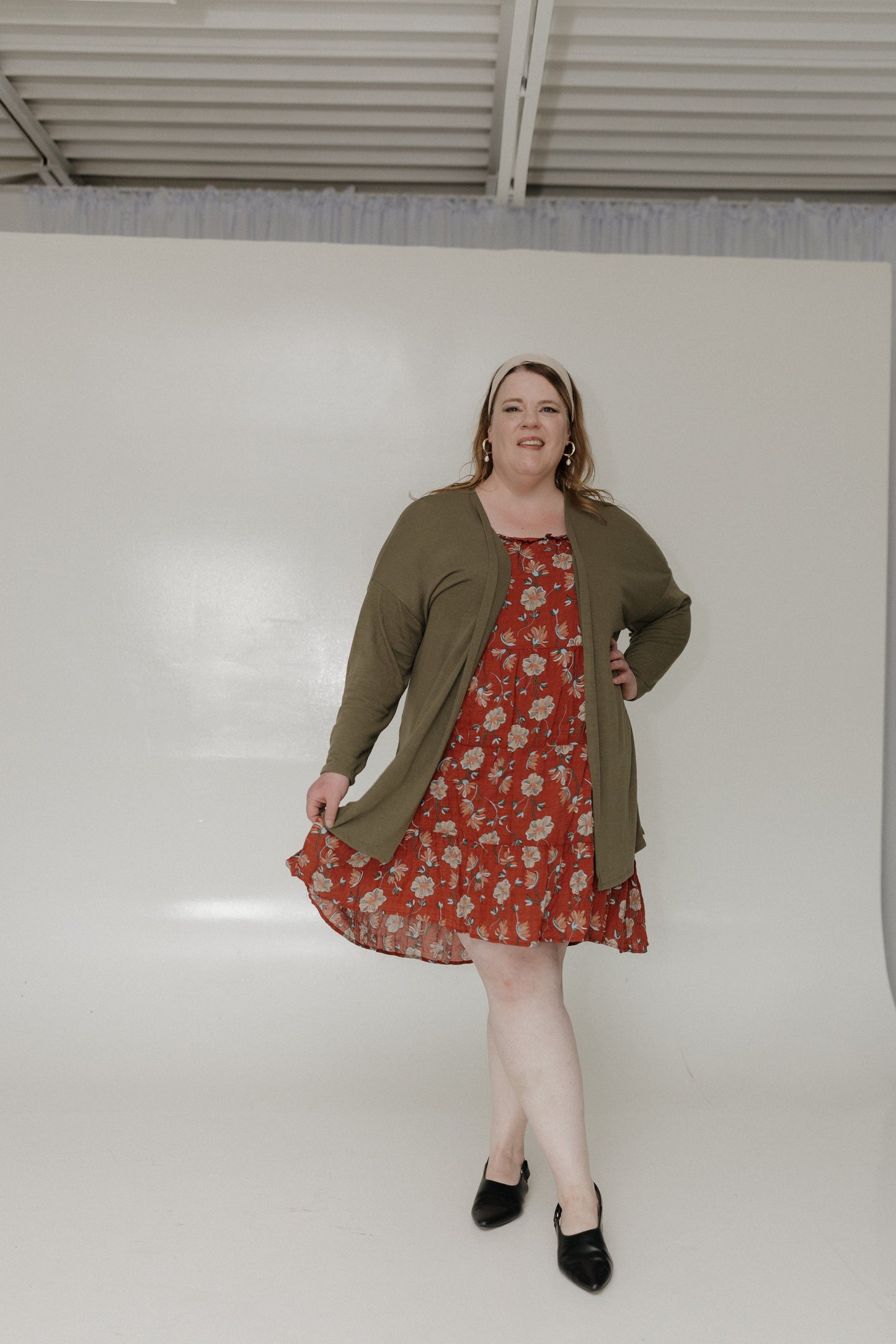 Woman wearing a floral dress and olive green cardigan against a plain background