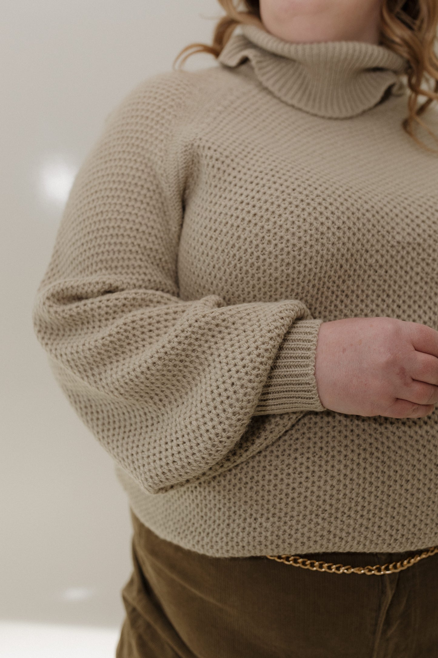 Person wearing a beige knitted sweater with a plain background