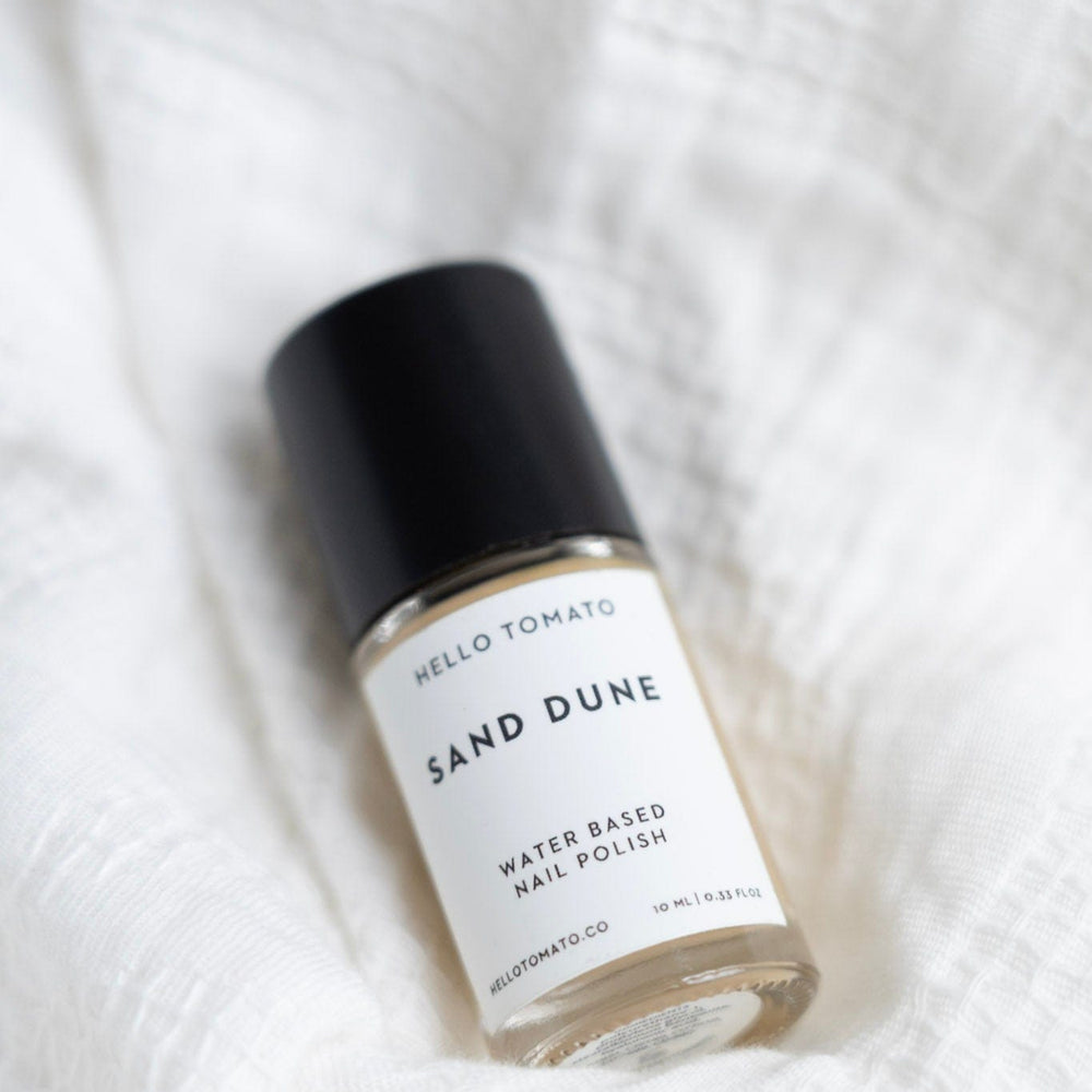Bottle of 'Sand Dune' water-based nail polish on a white textured background