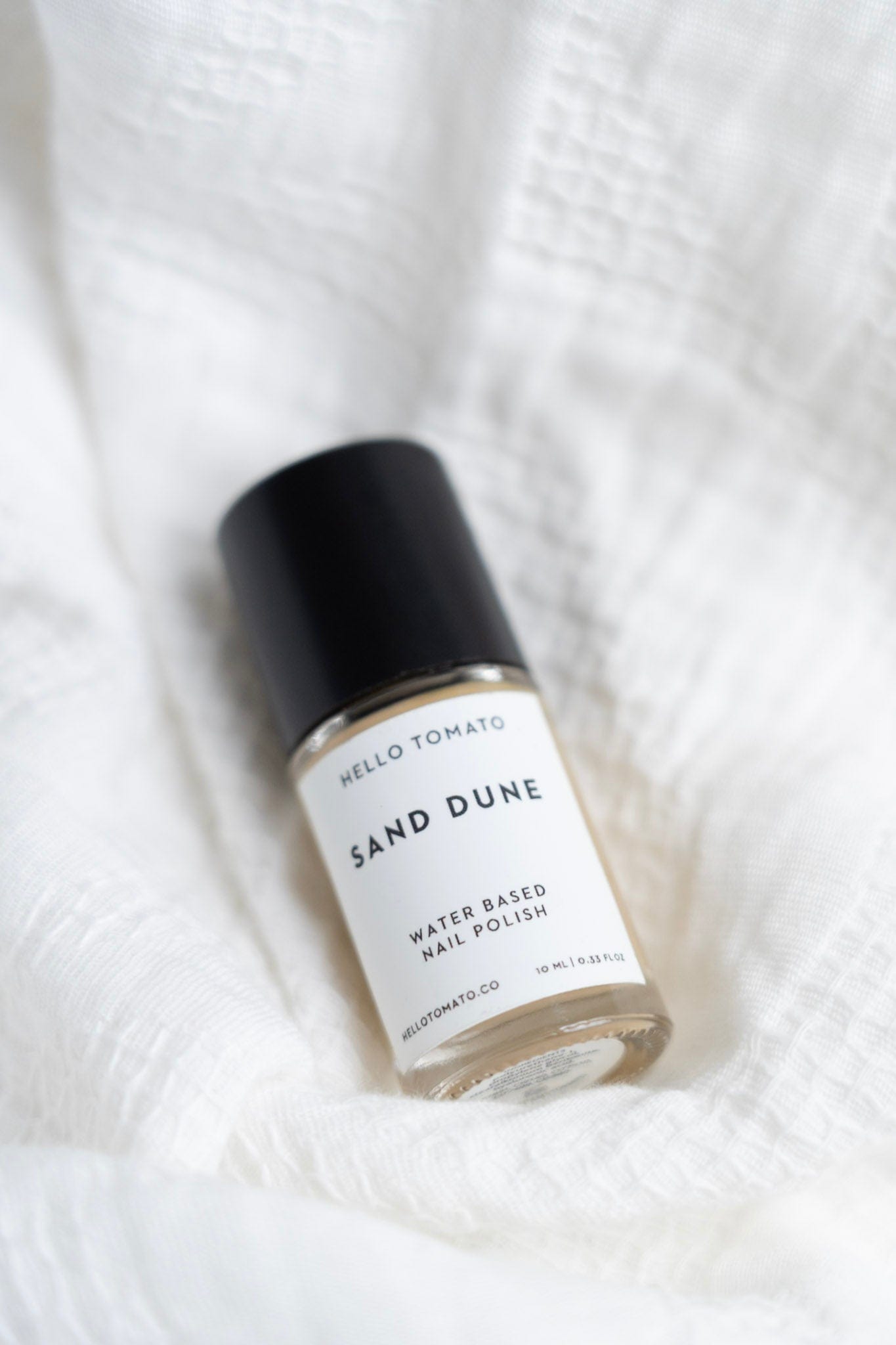 Bottle of 'Sand Dune' water-based nail polish on a white textured background