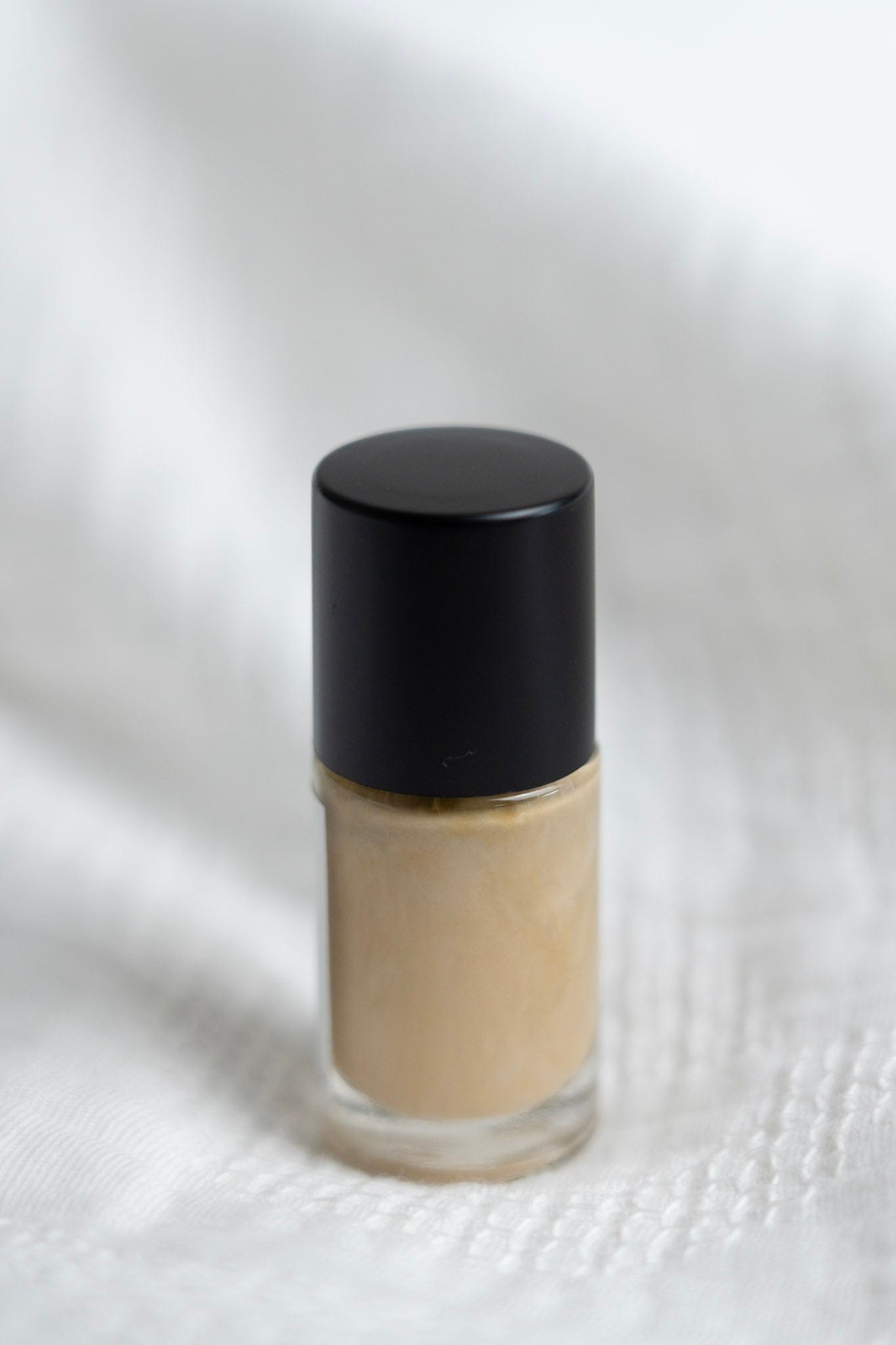 Small glass bottle with a black cap on a white textured background