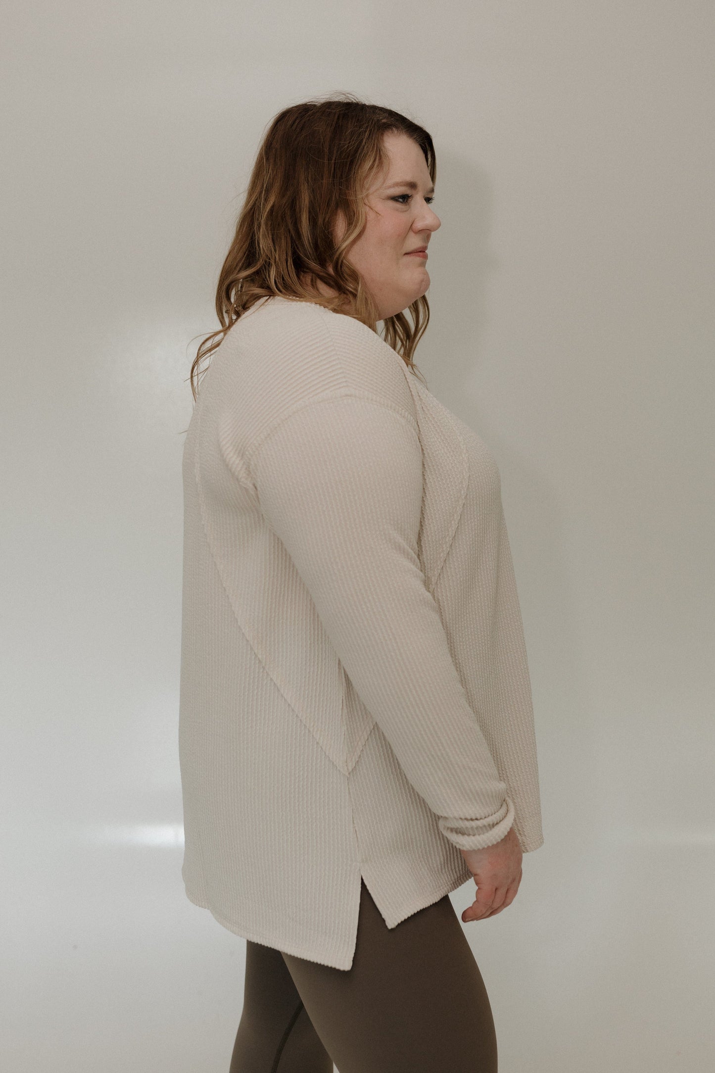 Woman wearing a sand long-sleeve top against a plain background
