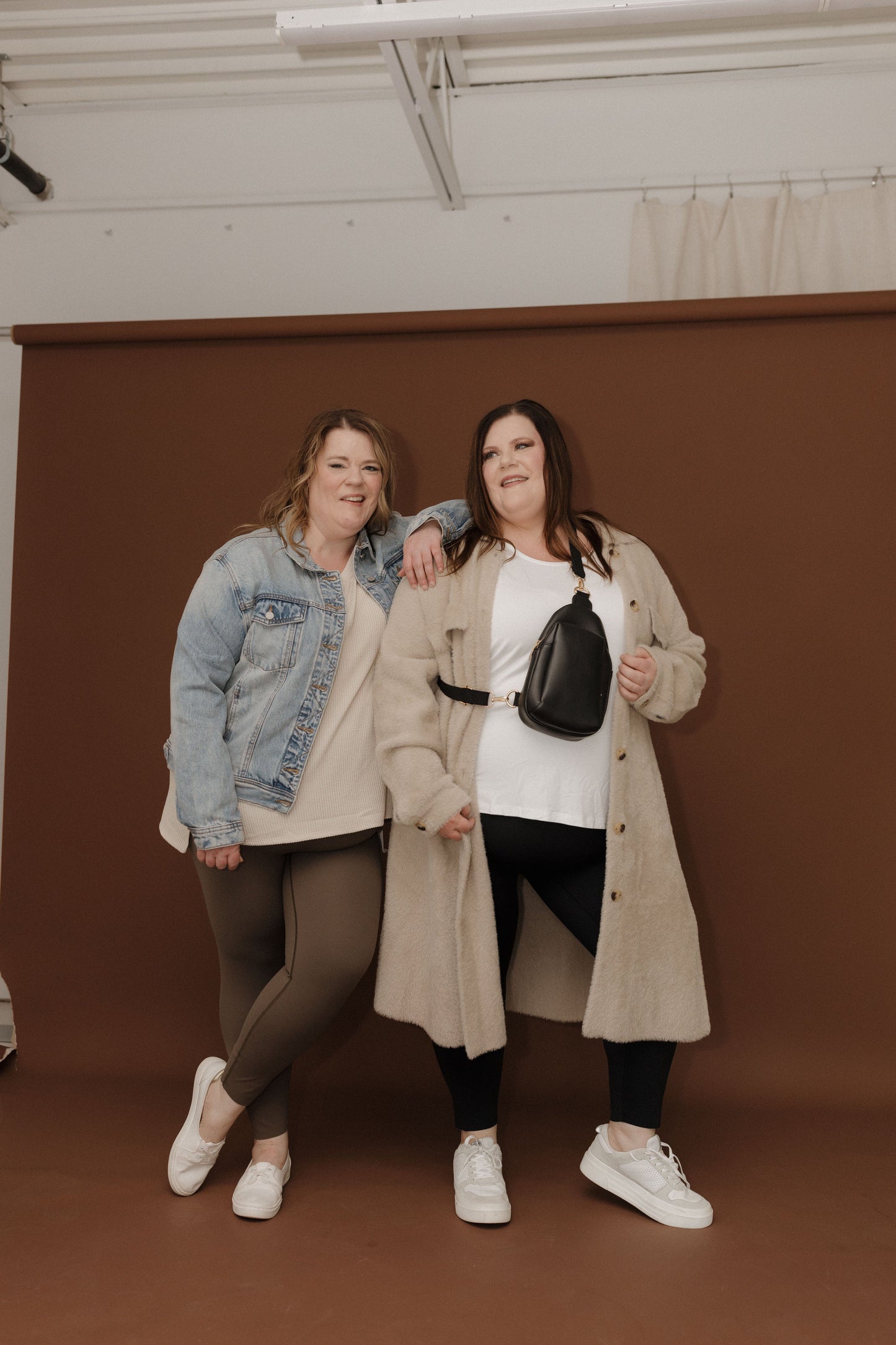 Two women posing together against a brown backdrop