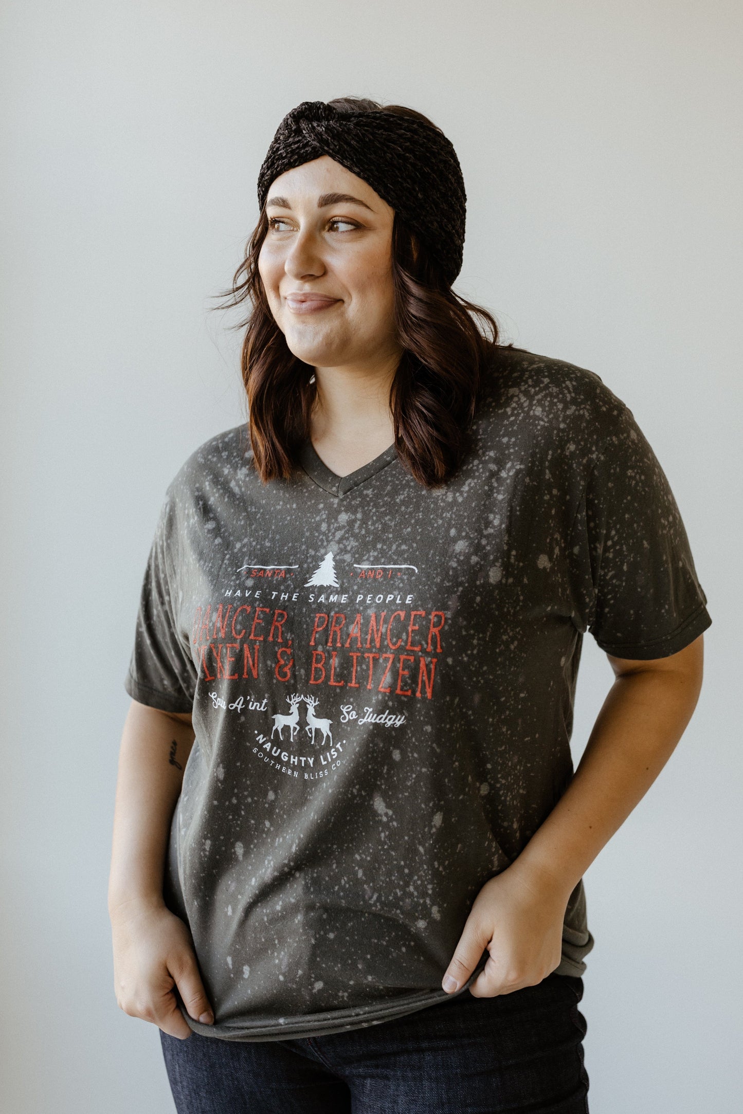 Person wearing a dark speckled t-shirt with festive reindeer names, showcasing their holiday spirit, and a black headband, standing against a light background.