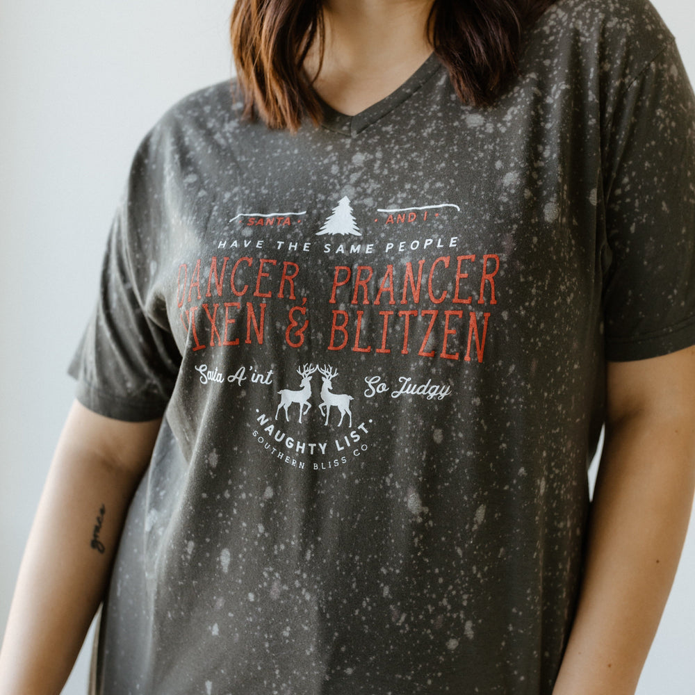 Person wearing a hand-bleached black speckled T-shirt featuring reindeer names and a Christmas theme design, perfect for showcasing holiday spirit.