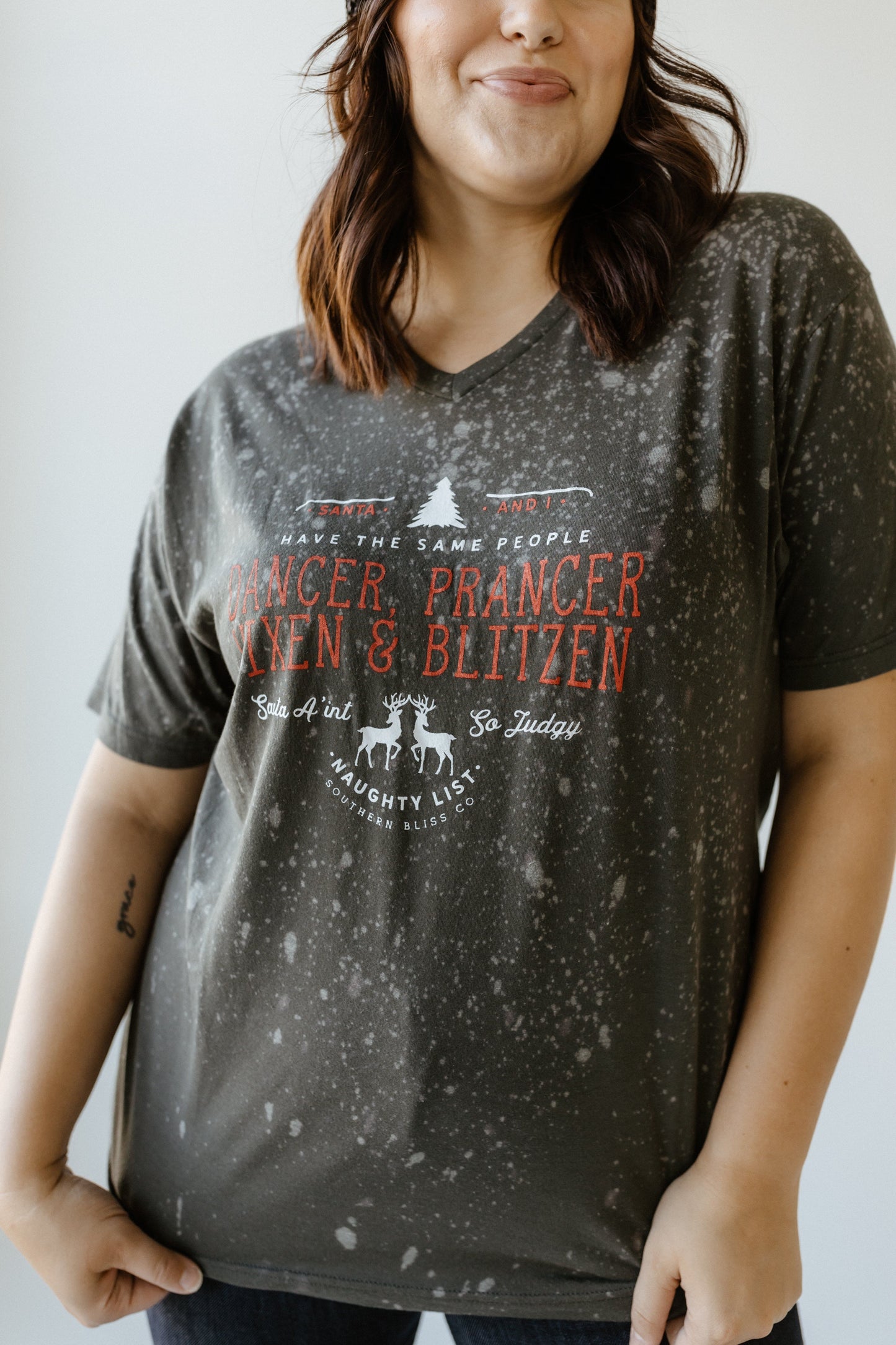 Person wearing a hand-bleached black speckled T-shirt featuring reindeer names and a Christmas theme design, perfect for showcasing holiday spirit.