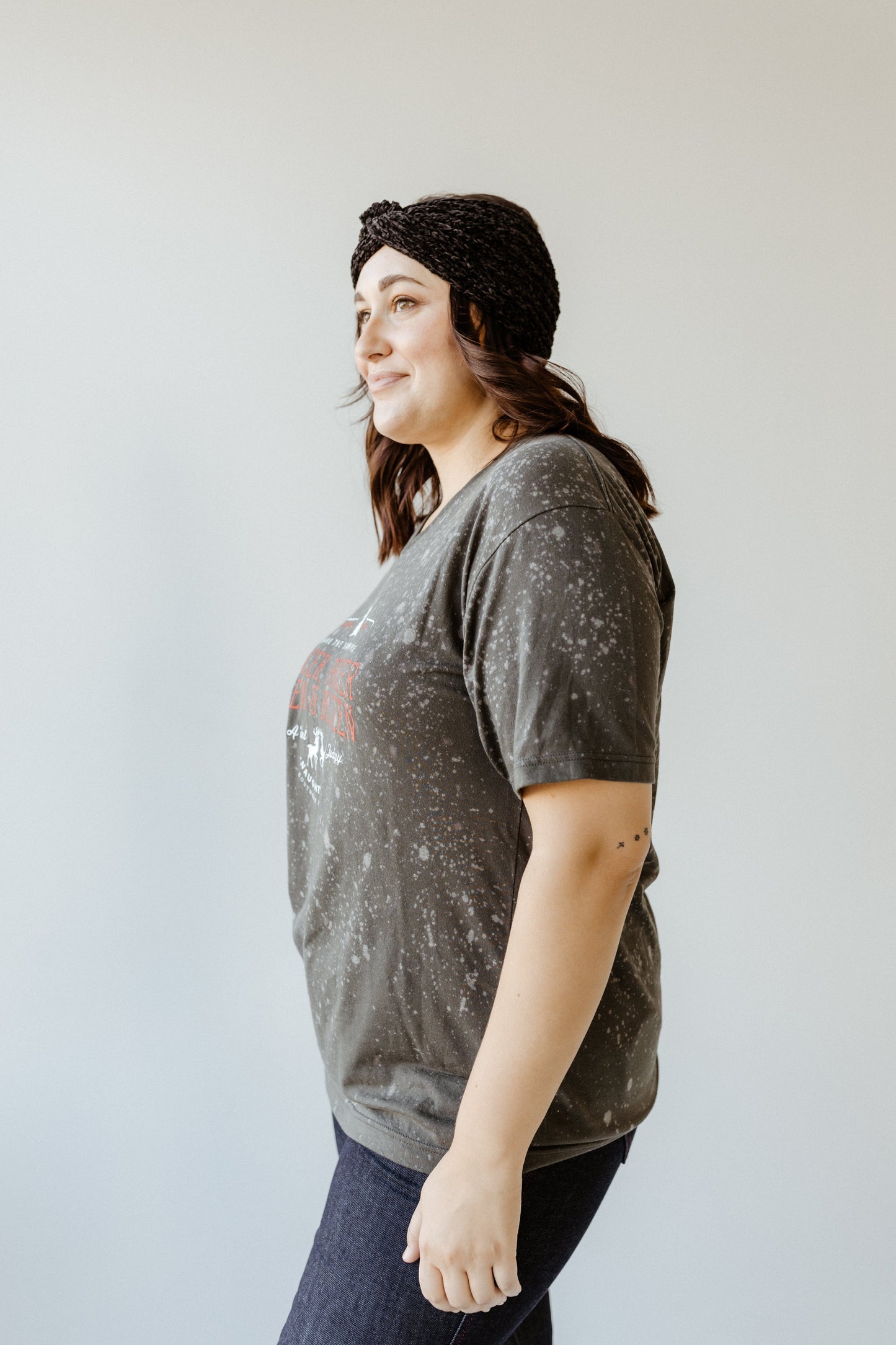 A person wearing a hand-bleached, speckled T-shirt and dark jeans stands against a plain light background, complemented by a dark headband.