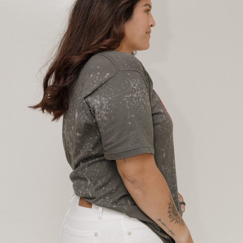 Woman wearing a gray t-shirt with white splatter pattern against a plain background