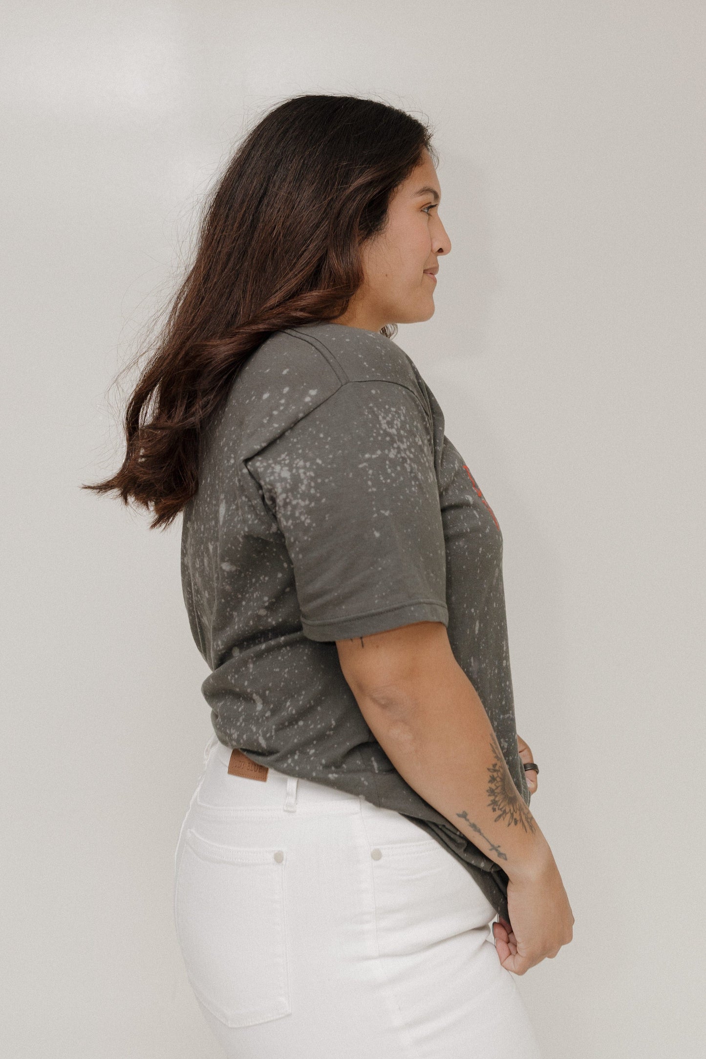 Woman wearing a gray t-shirt with white splatter pattern against a plain background