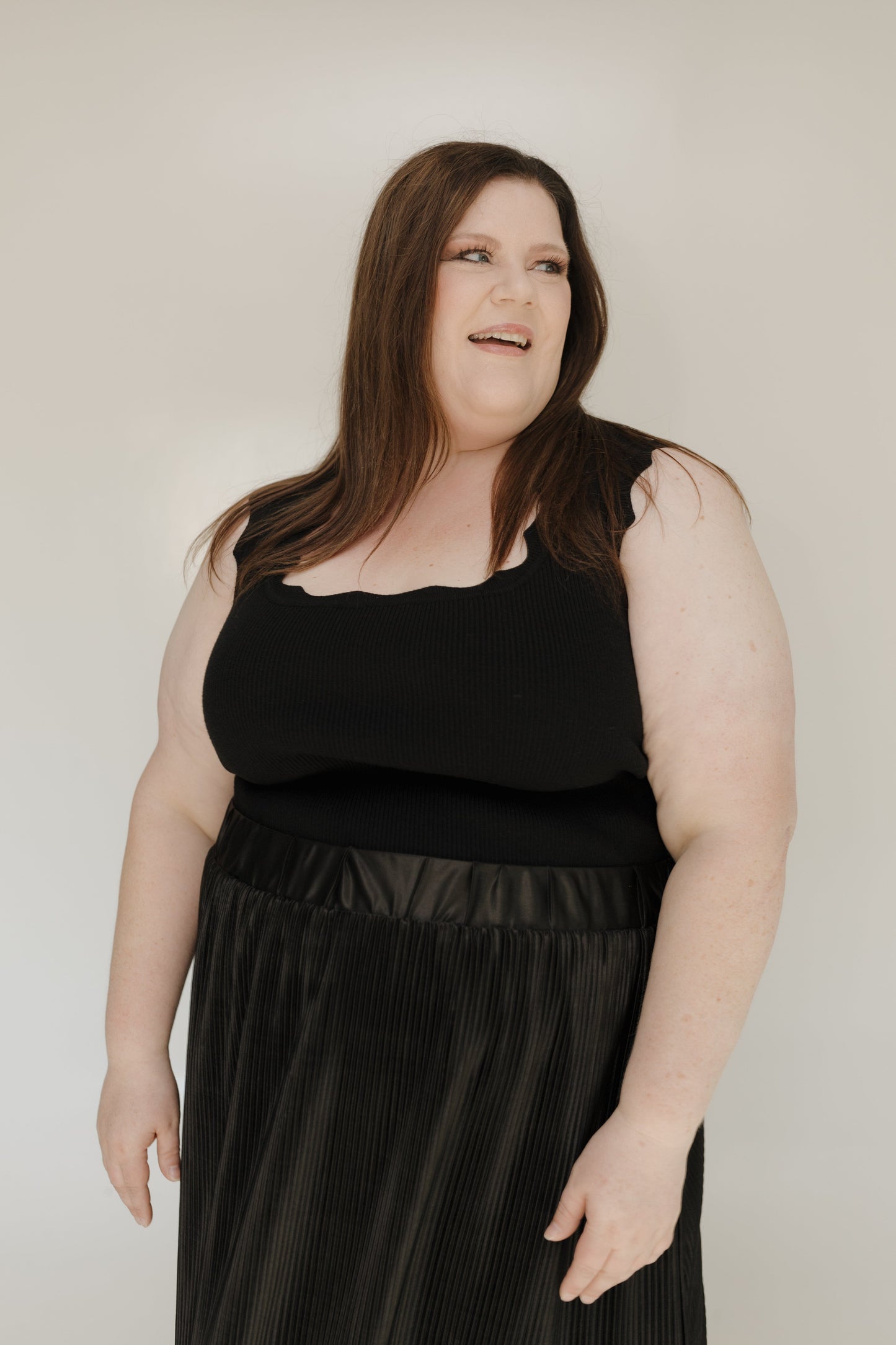 Woman wearing a black sleeveless top and black skirt against a plain background