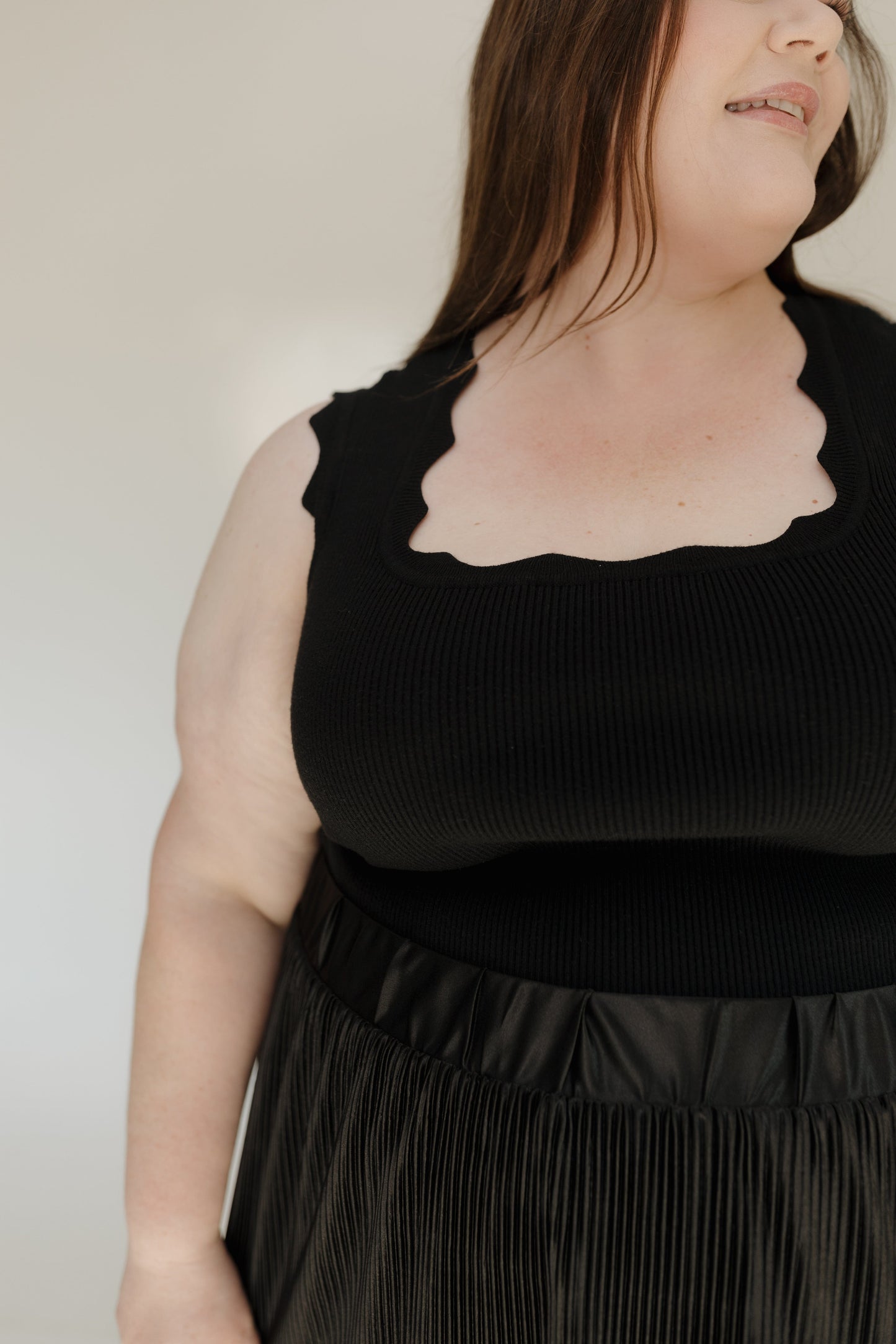 Person wearing a black sleeveless top with sheer neckline against a neutral background