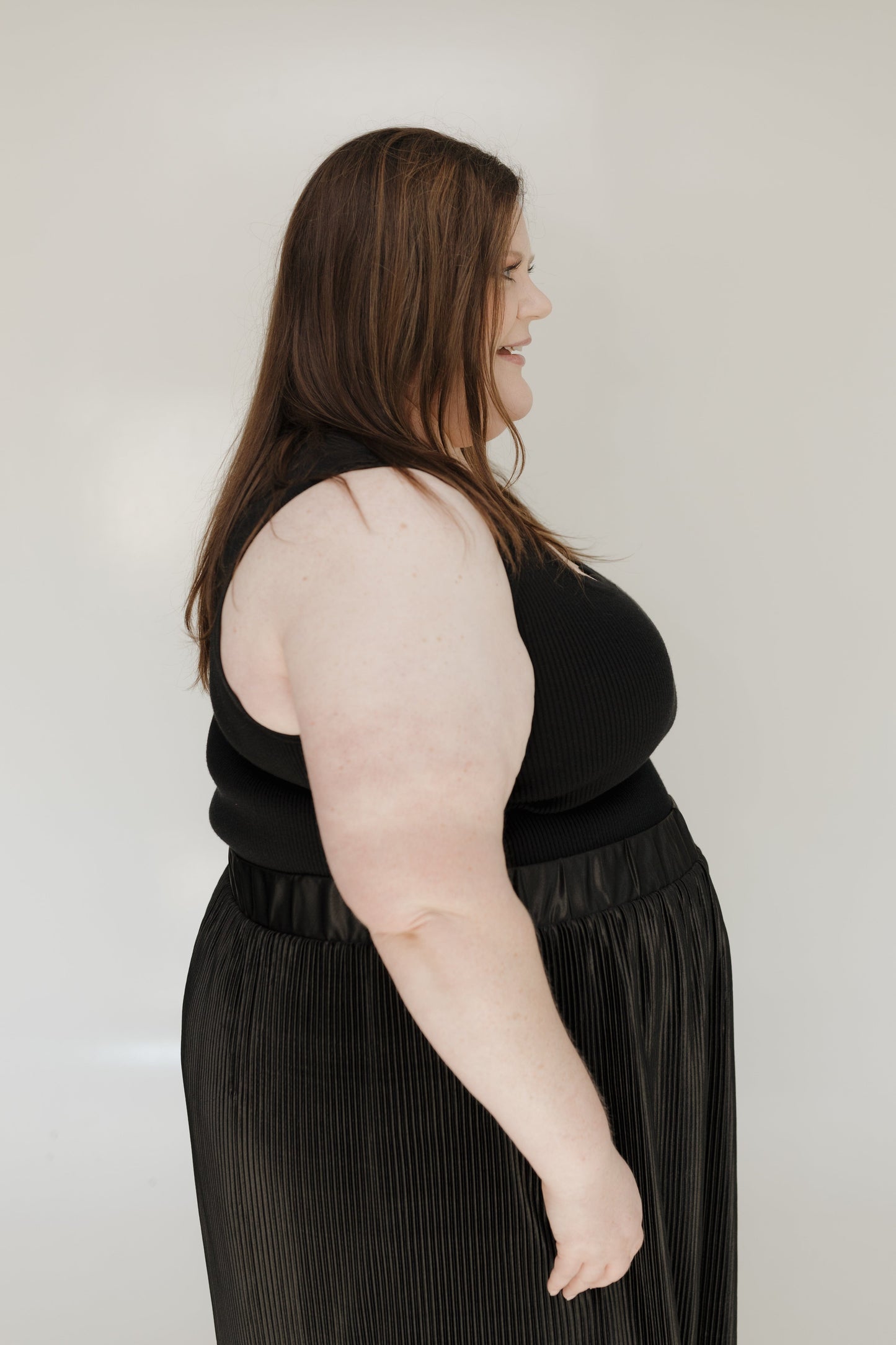 Woman wearing a black sleeveless top and black skirt against a plain background
