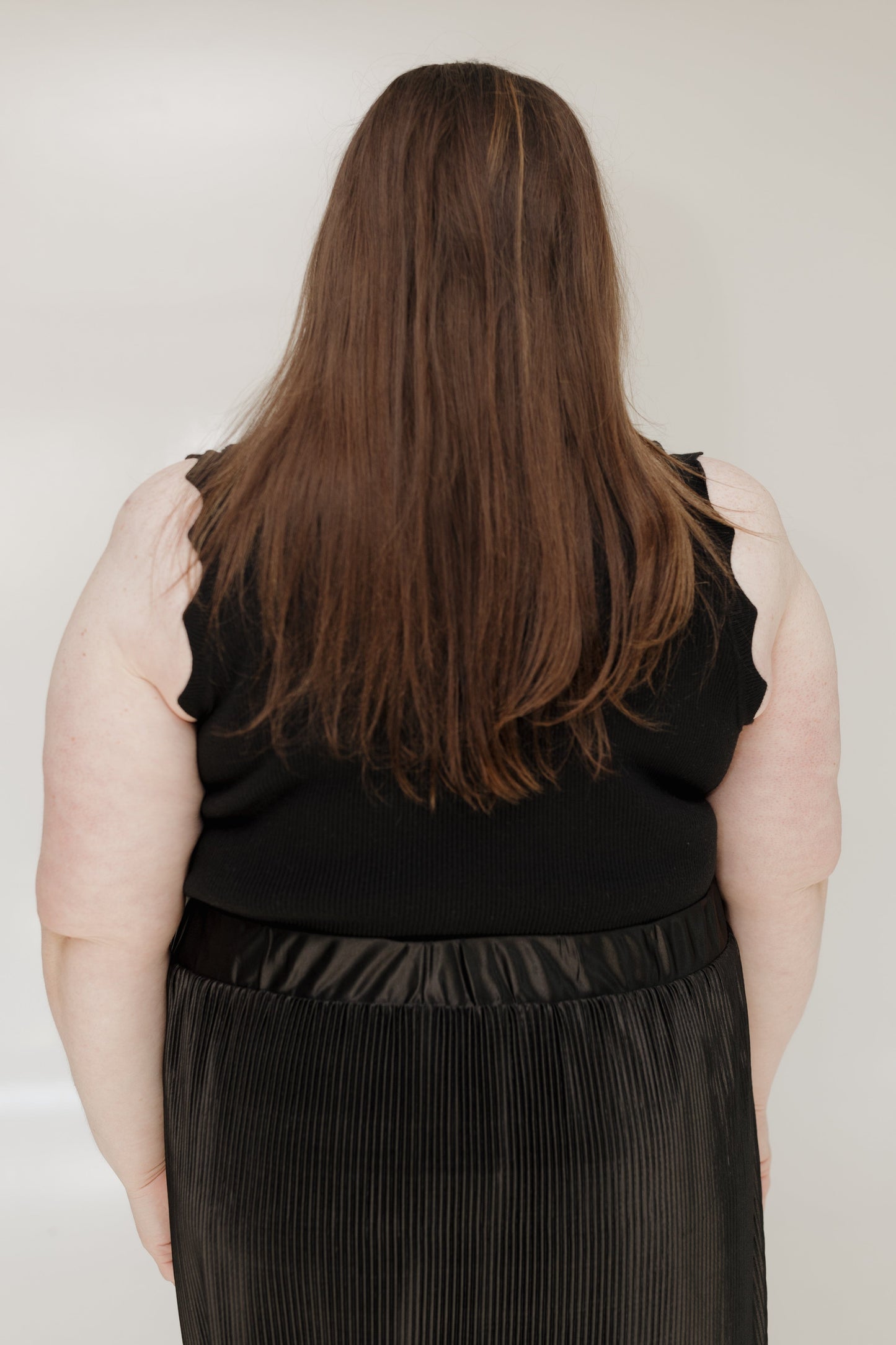 Person wearing a black sleeveless top and pleated skirt from behind on a plain background