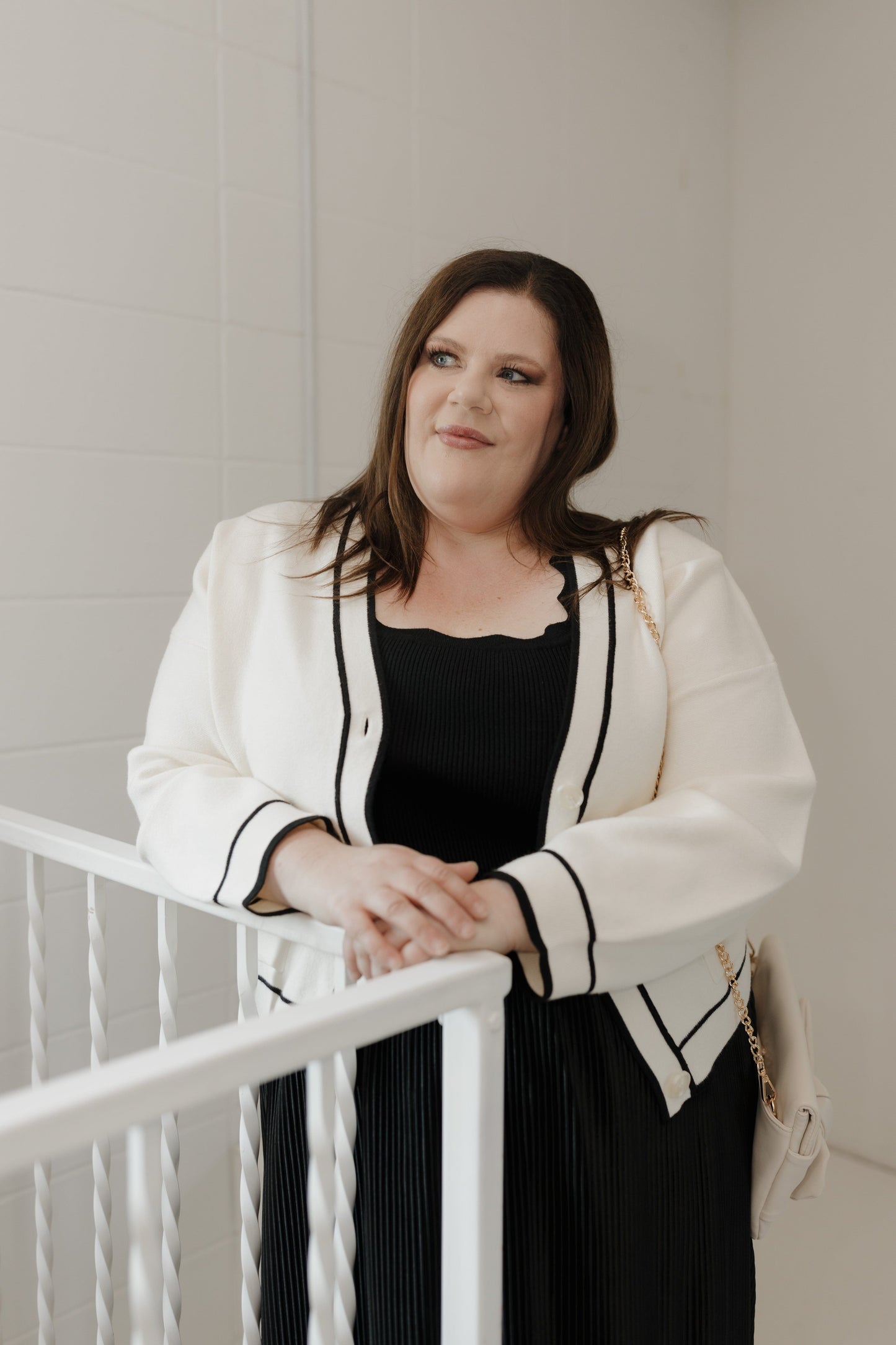 Woman in a white blazer and black dress standing on a staircase.