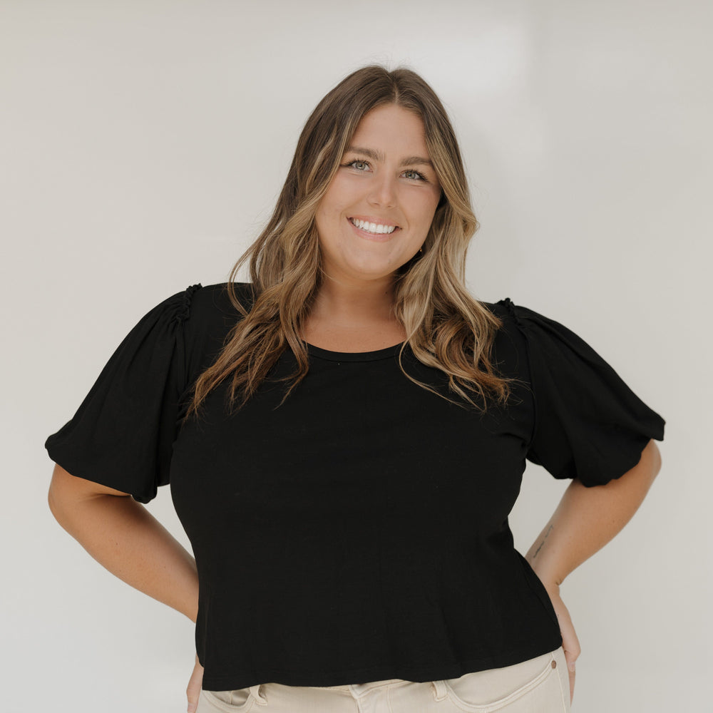 Woman wearing a black top with puffed sleeves against a white wall