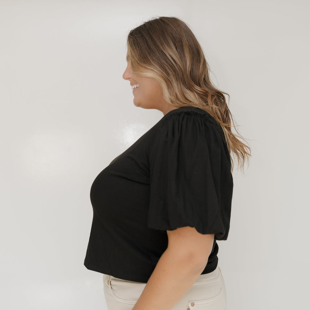 Woman wearing a black top and beige pants against a white background