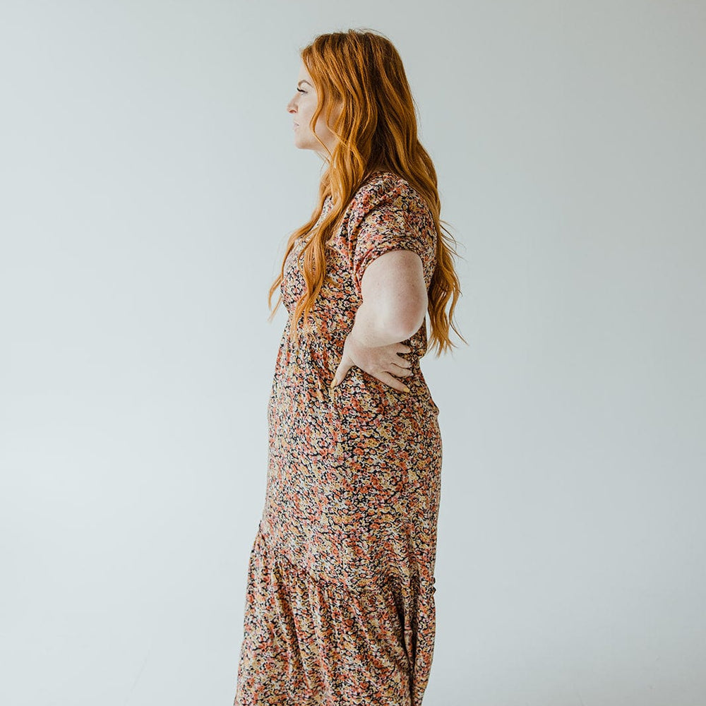 A person with long red hair is wearing the Mikarose Scoop Neck Midi Length Dress with Kick Hem in Autumn Bouquet, standing in profile against a plain white background.