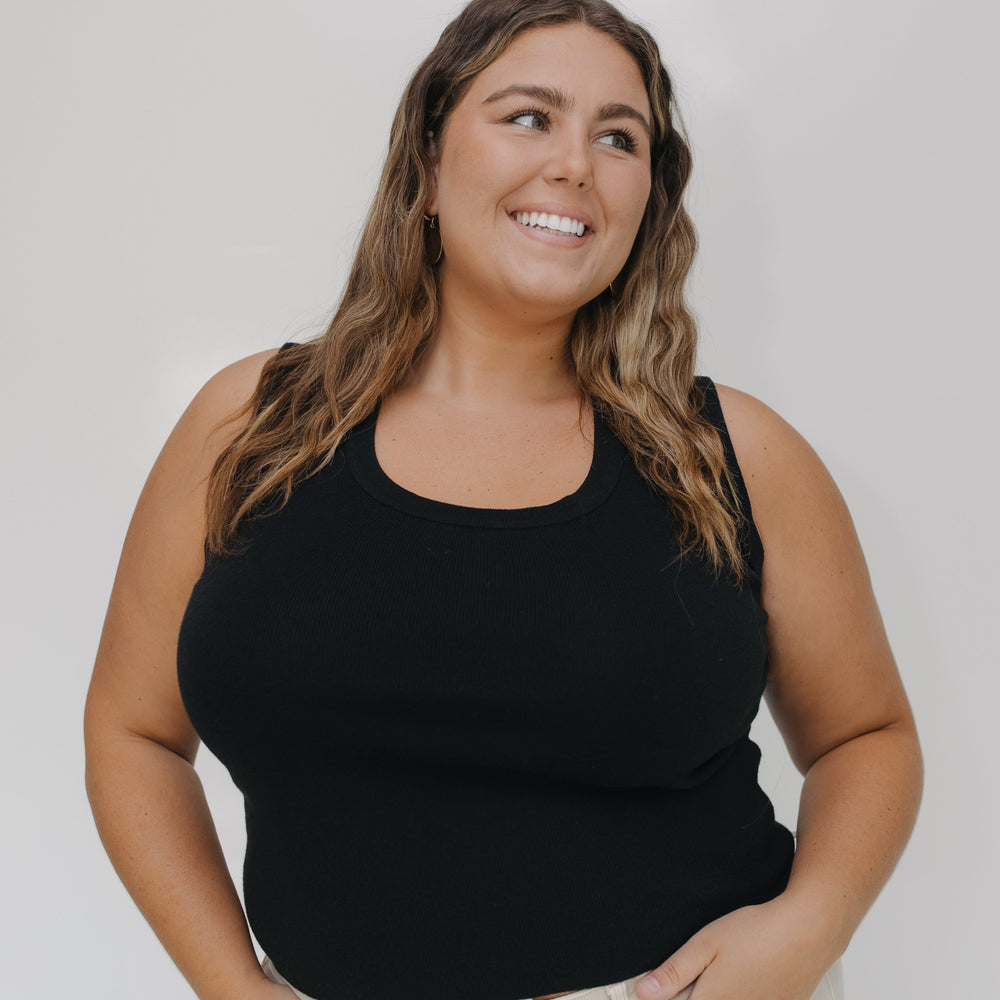Woman wearing a black tank top and beige pants against a white background