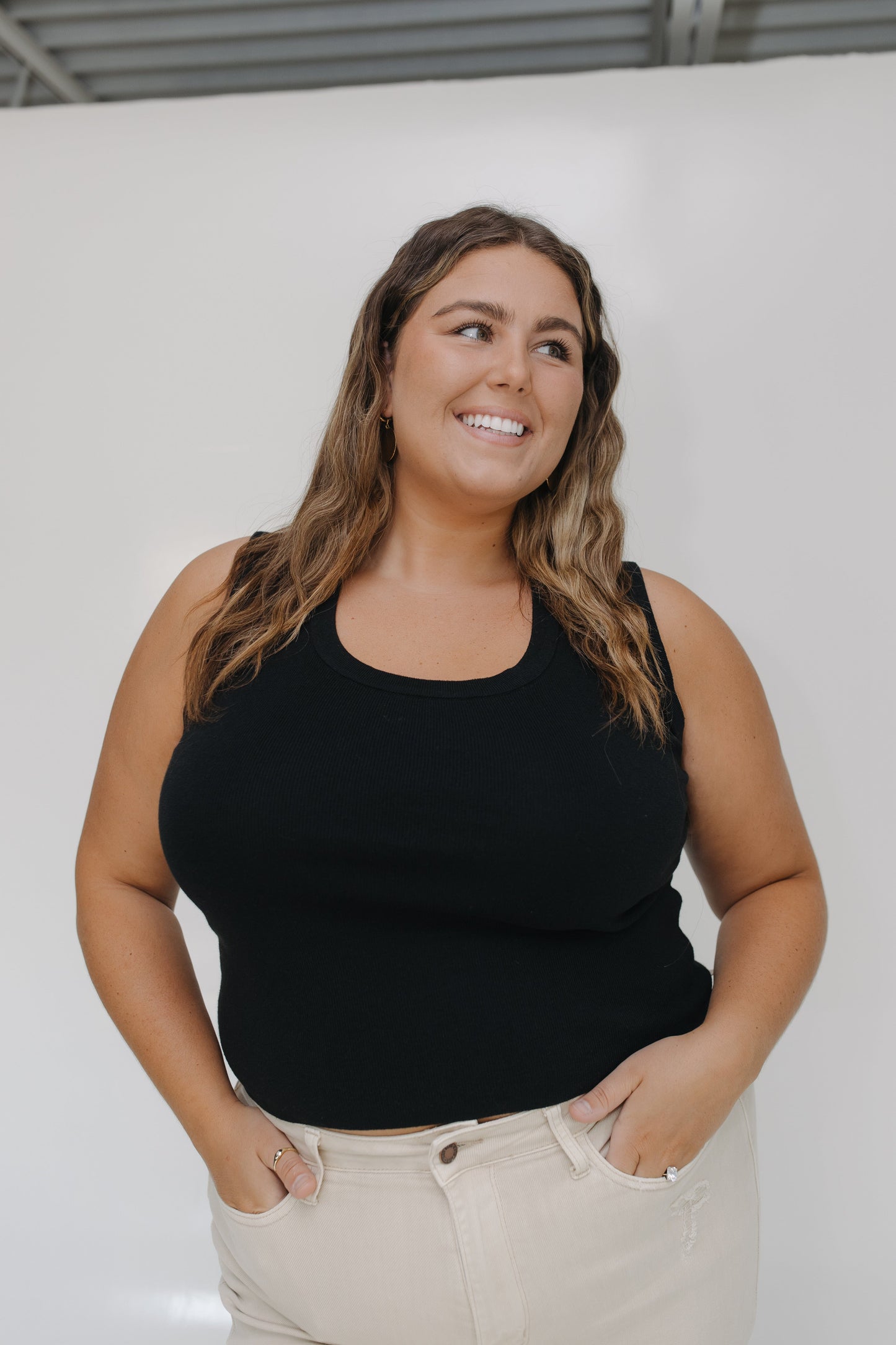 Woman wearing a black tank top and beige pants against a white background