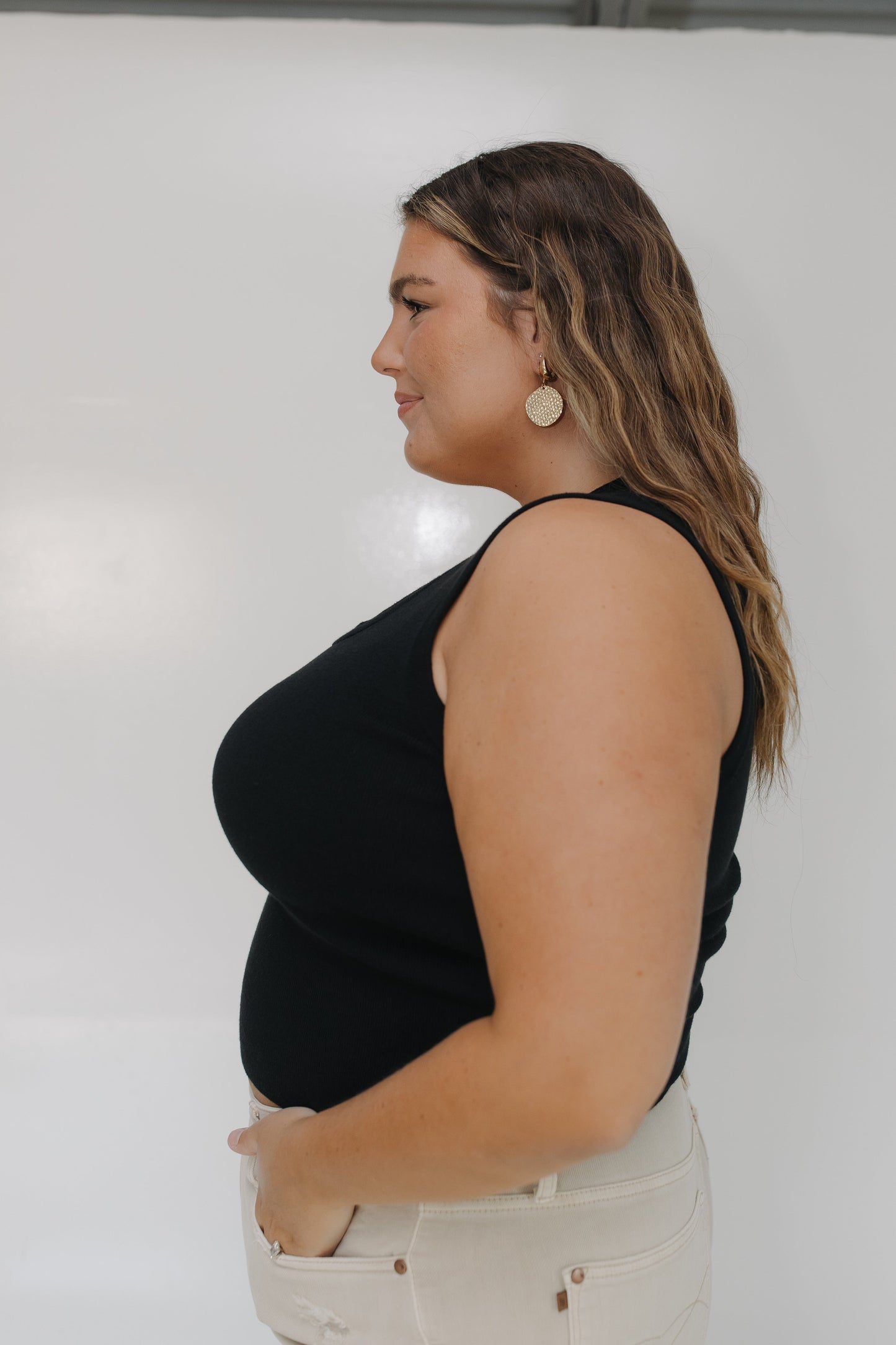 Woman wearing a black sleeveless top and beige pants against a white background