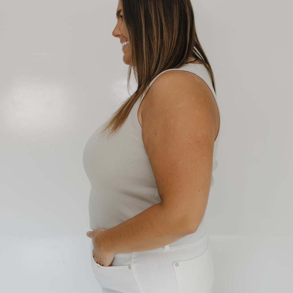 Woman wearing a white sleeveless top and white pants against a plain background