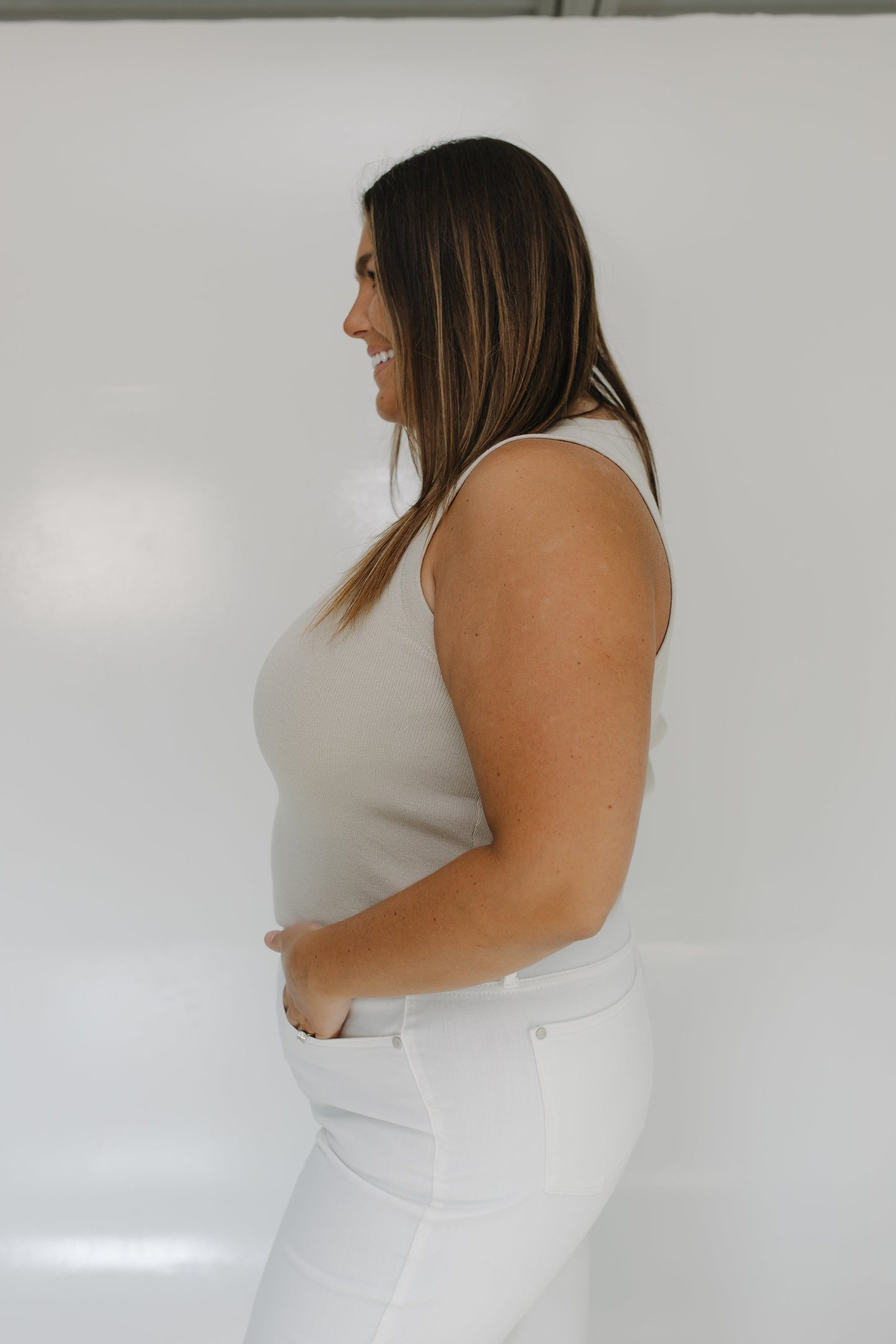 Woman wearing a white sleeveless top and white pants against a plain background