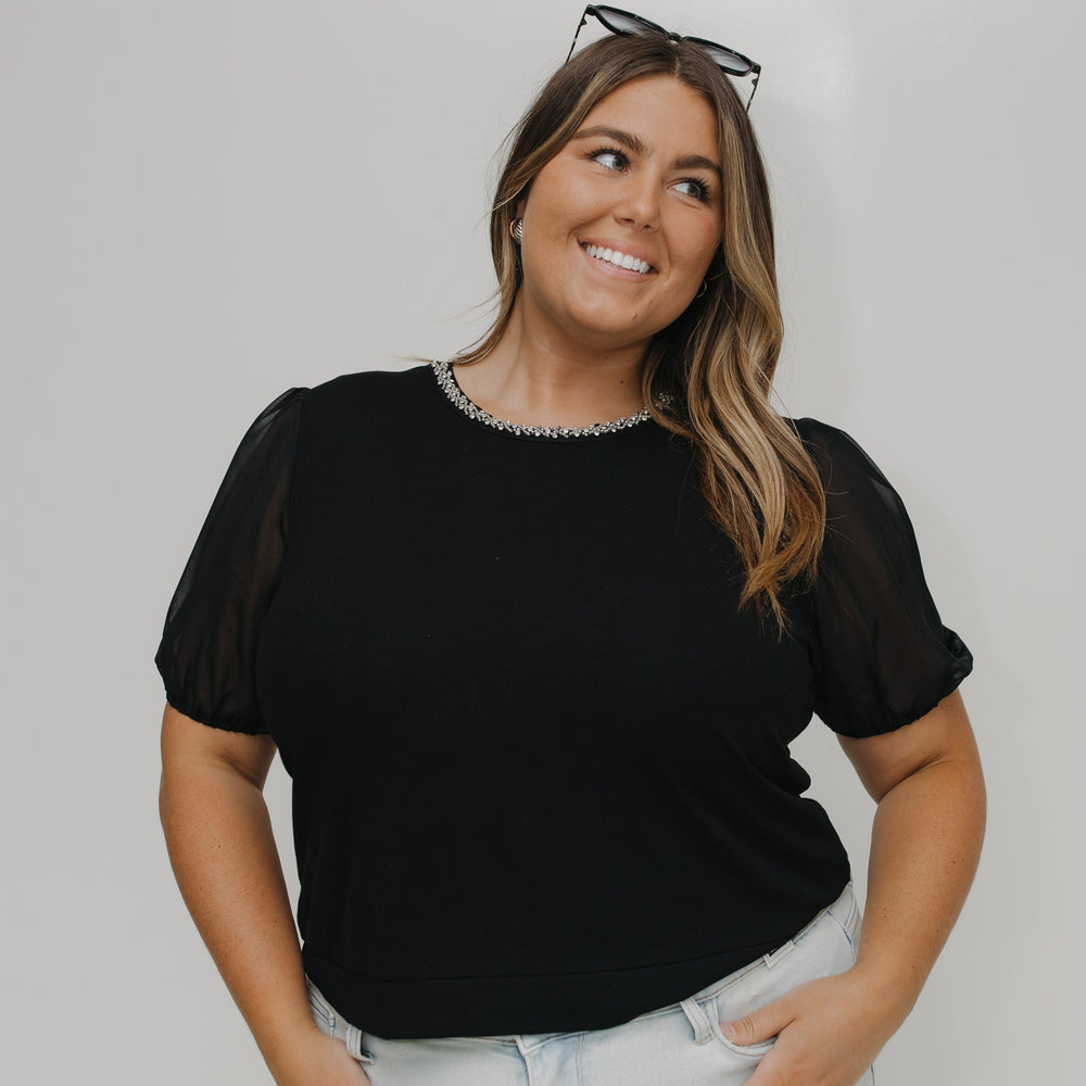 Woman wearing a black top with sheer sleeves against a white background