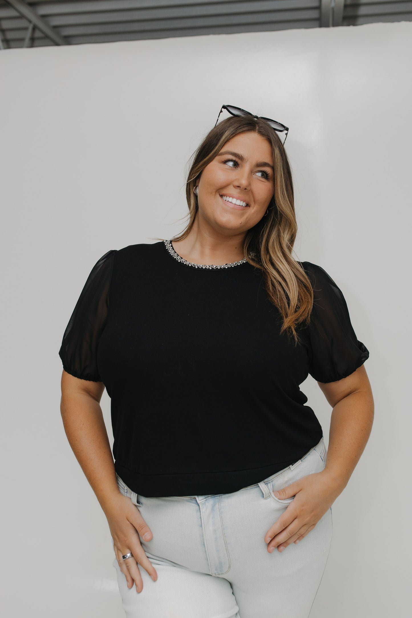 Woman wearing a black top with sheer sleeves against a white background