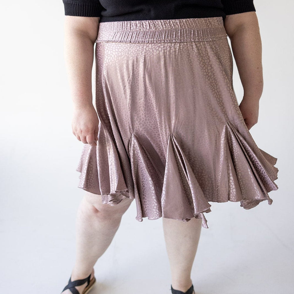 A person wearing a black top, a dusty rose tiered mini skirt, and black sandals stands against a plain background.